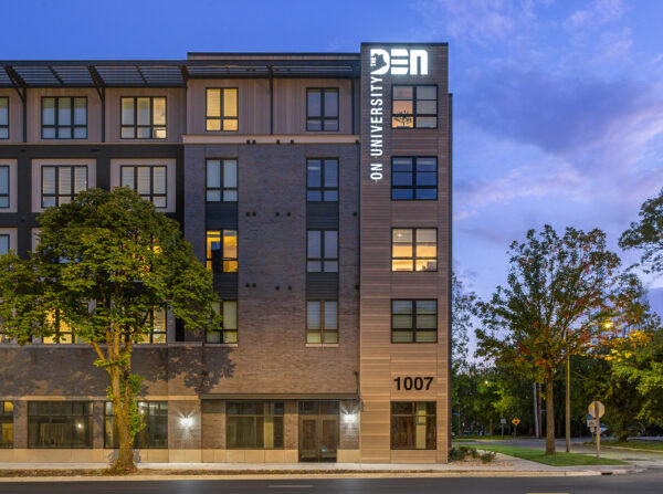 Den on University facade at dusk.