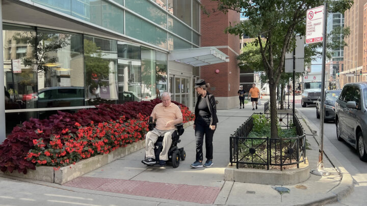 Jack Catlin in wheelchair with Liz Zaverdas walking alongside at Access Living entrance.