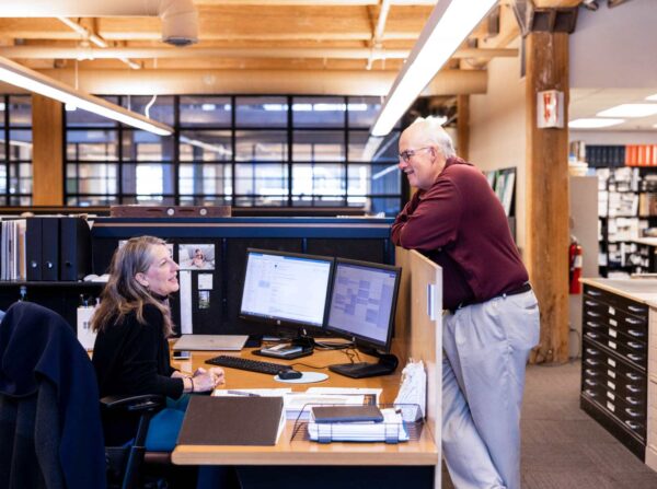 Mark Small and Liz Zaverdas talking at her desk.