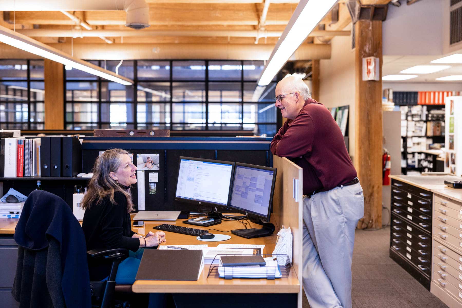 Mark Small and Liz Zaverdas talking at her desk.