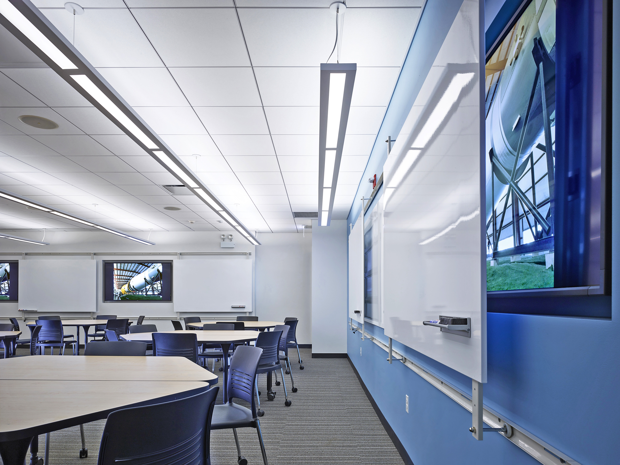 Peer-to-peer classroom with modular desks, monitors and sliding whiteboards on the walls.