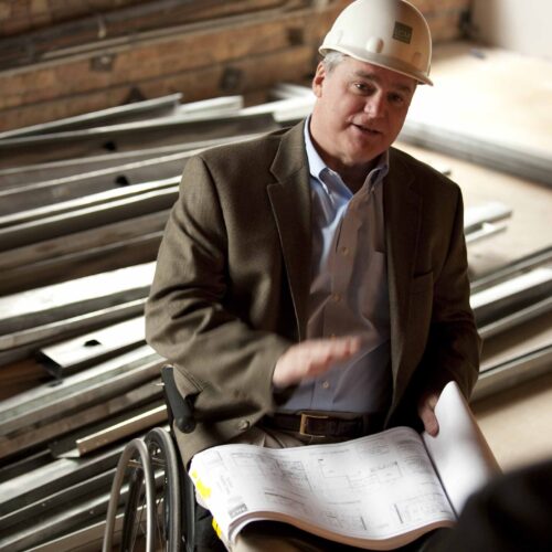 LCM co-founder Jack Catlin on work site in wheelchair wearing and hard hat.