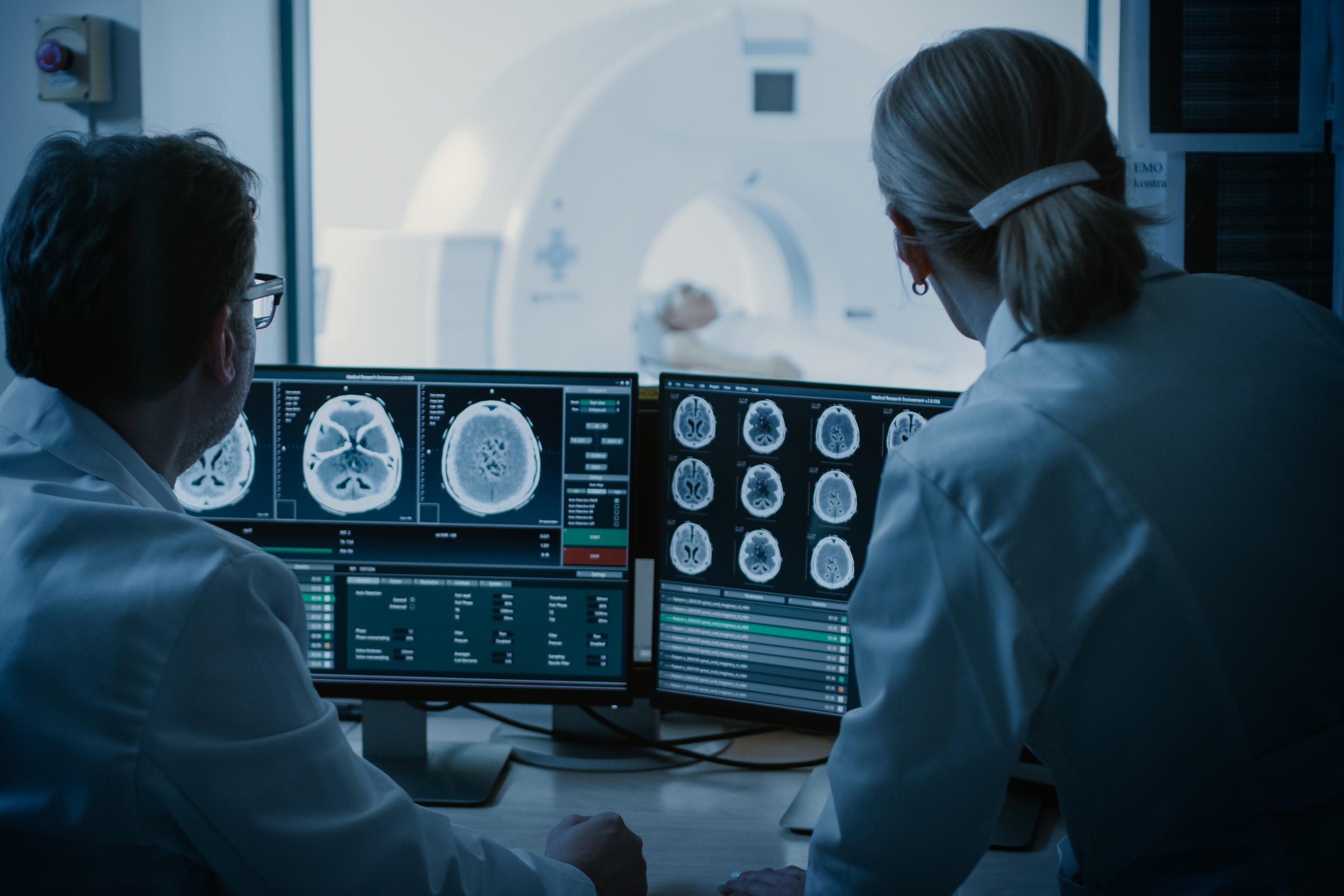 Two doctors reviewing the results of a CT scan with the patient in the background.